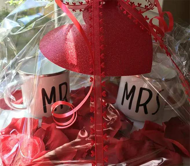 Hochzeitsgeschenk mit zwei Tassen, roter Dekoration und Schleifen in transparenter Geschenkfolie